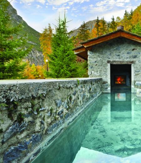 Piscina termale con vista montagna e fuoco acceso.