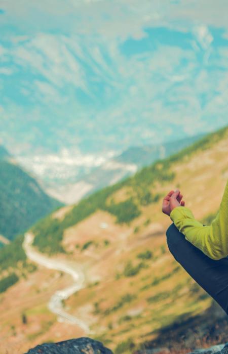 Donna medita in montagna, natura avvolgente e pace interiore.