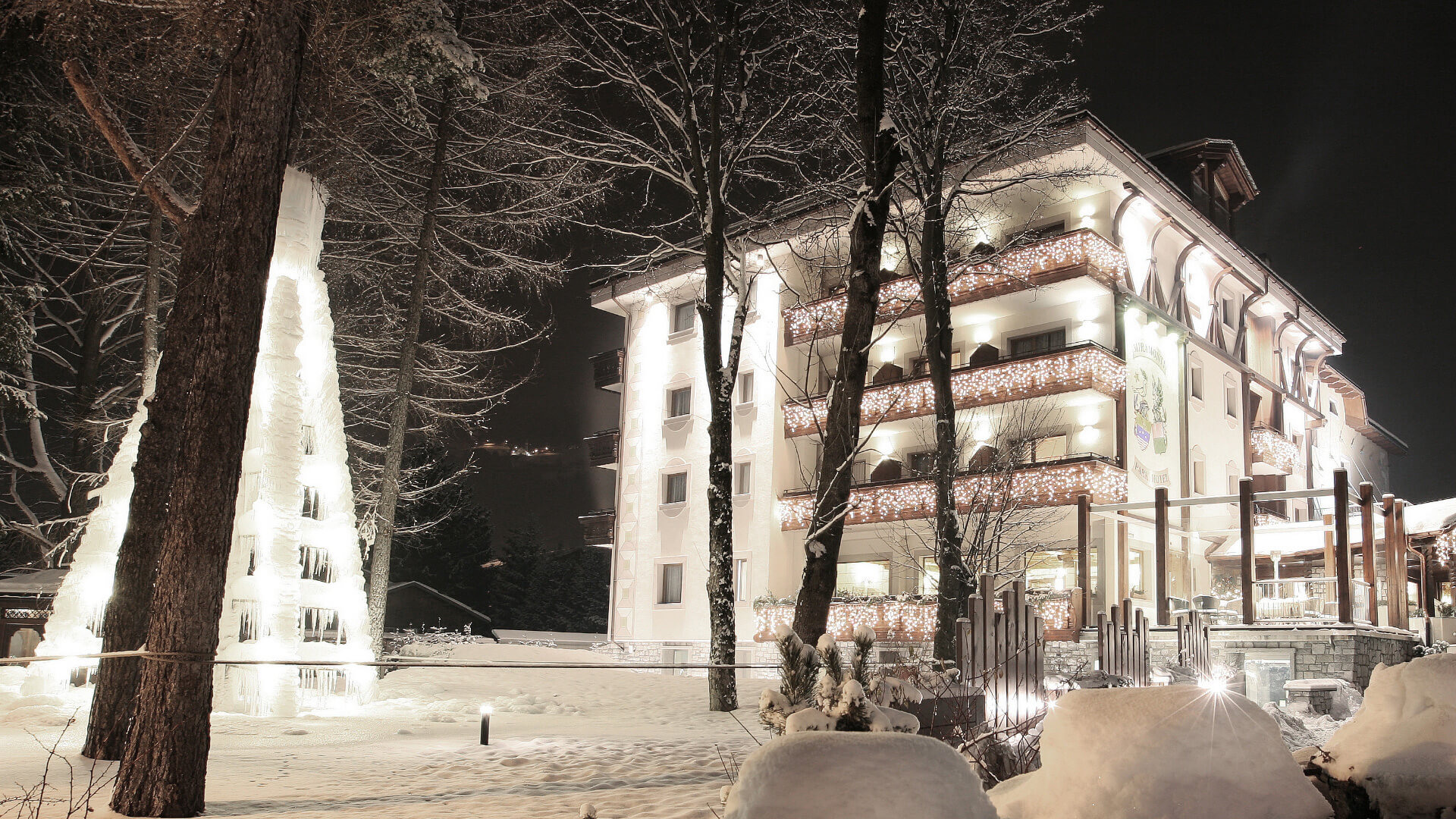 Hotel innevato di notte con luci natalizie e albero di ghiaccio.