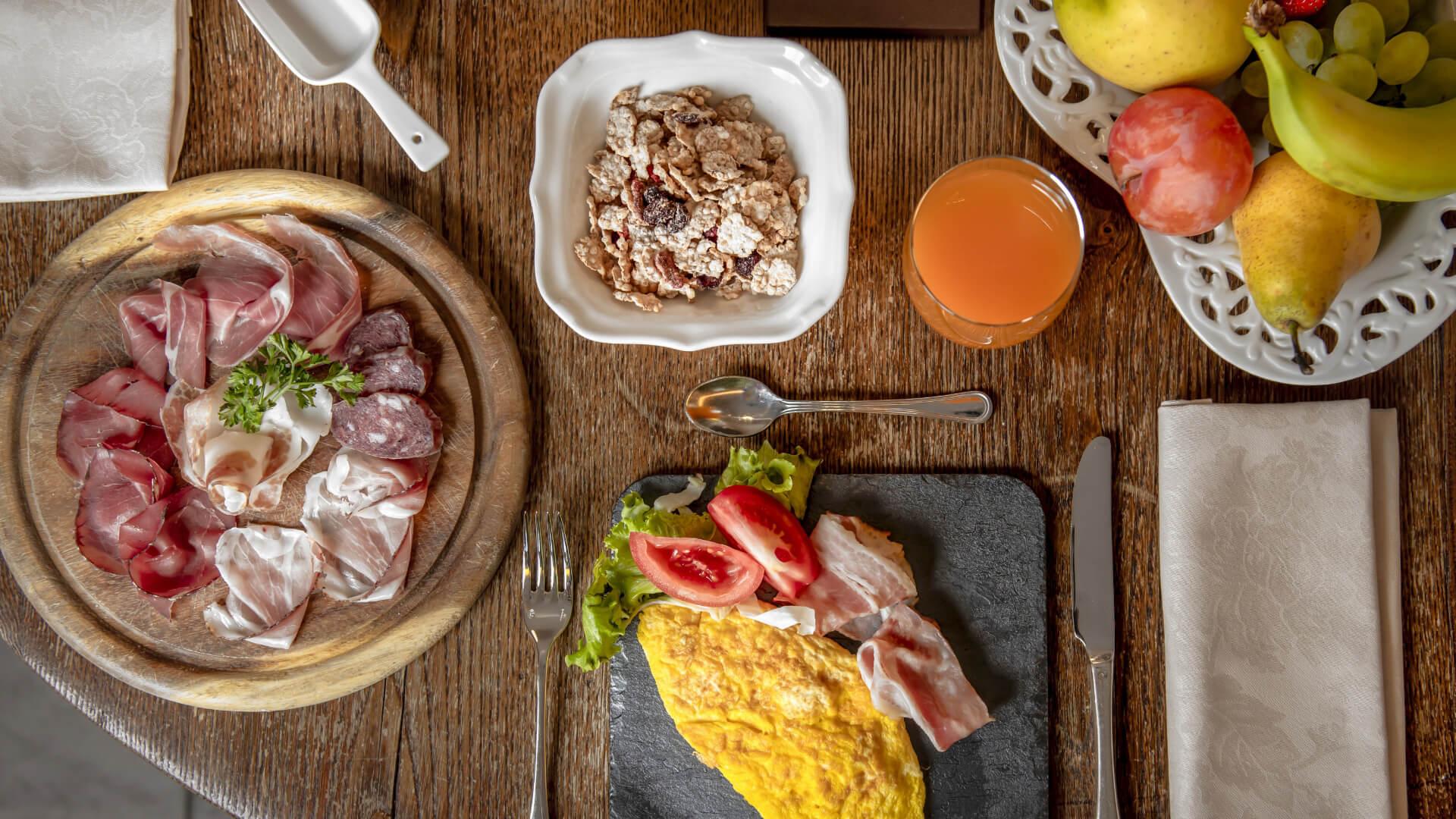 Colazione con affettati, omelette, cereali, frutta fresca e succo d'arancia.