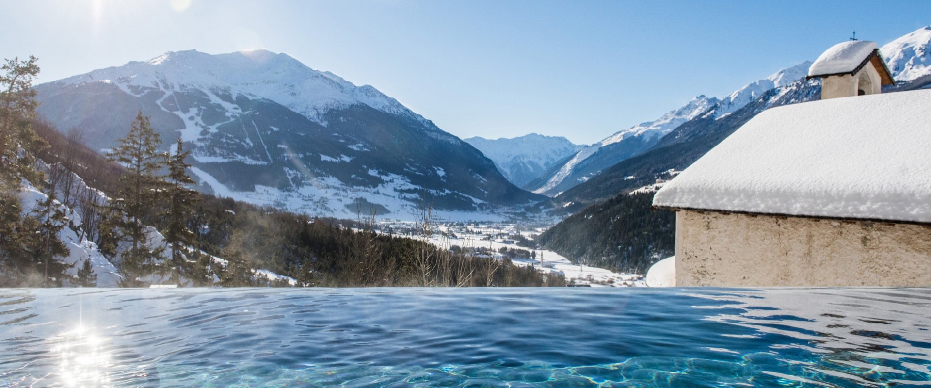 Piscina con vista panoramica sulle montagne innevate e la valle.