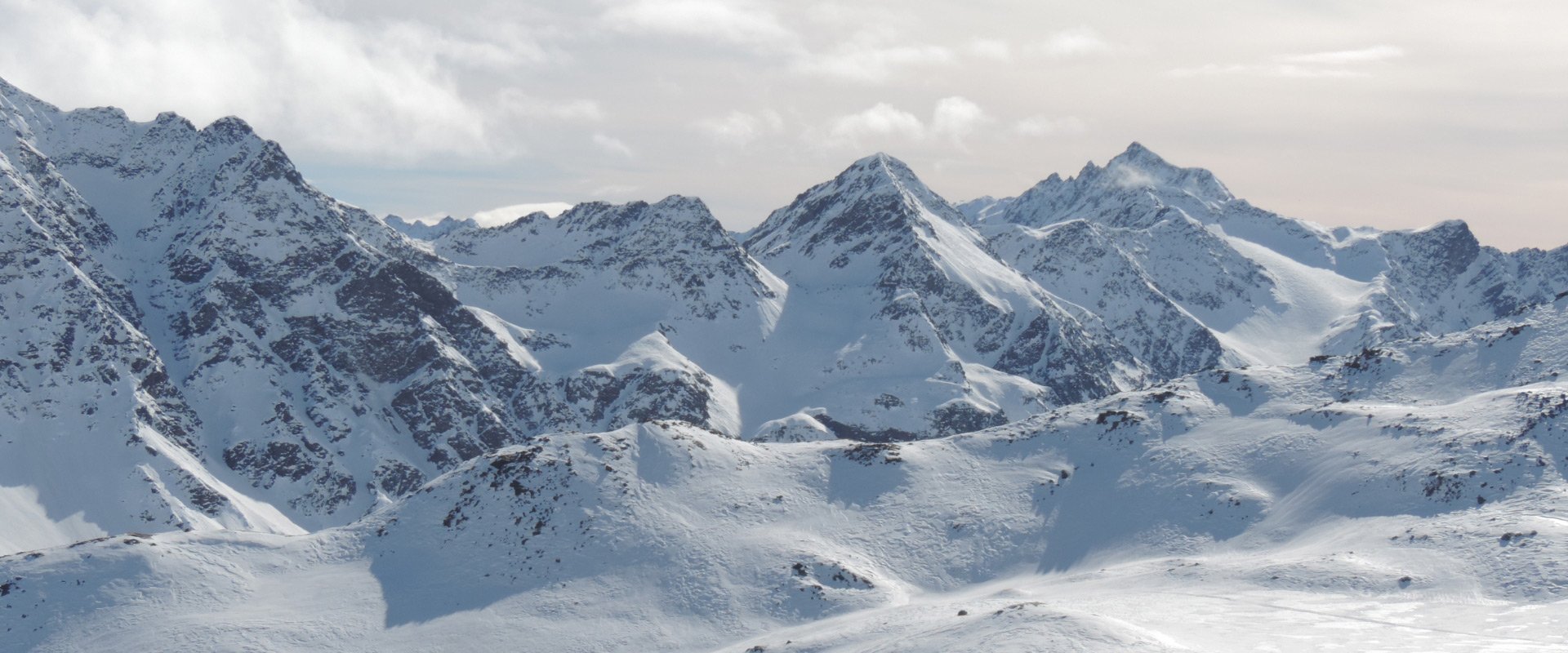 Paesaggio montano innevato con cime frastagliate e cielo parzialmente nuvoloso.