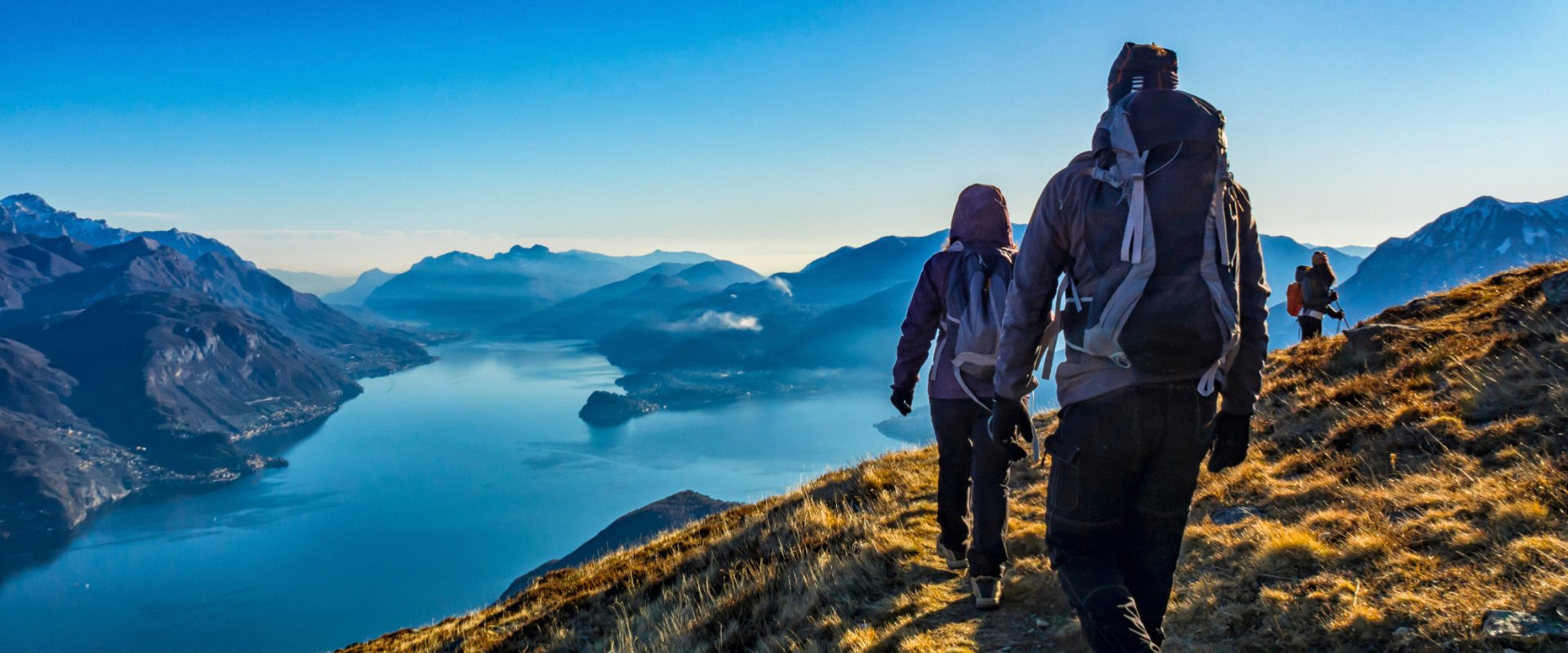 Escursionisti camminano lungo un sentiero di montagna con vista su un lago.