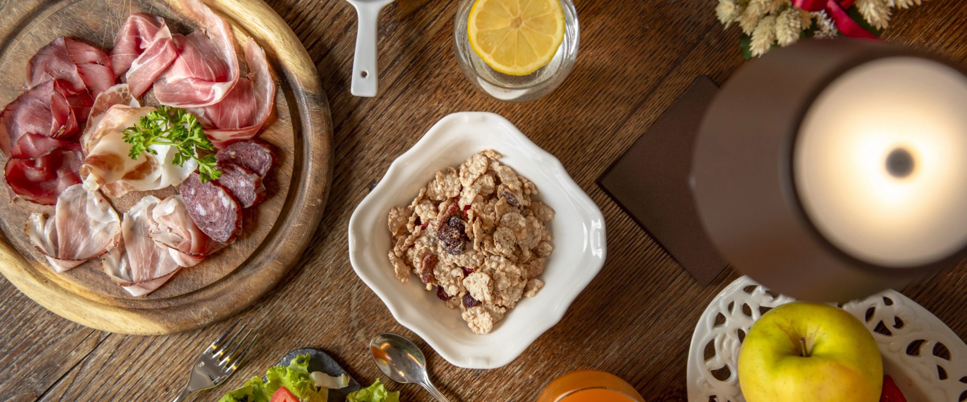 Tagliere di salumi, cereali, limonata e mela su un tavolo di legno.