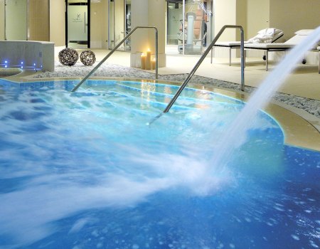 Piscina termale con idromassaggio, candele accese e area relax con lettini.