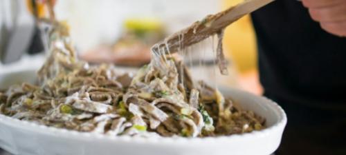 Pasta cremosa con verdure fresche, mescolata con formaggio filante in una ciotola bianca.