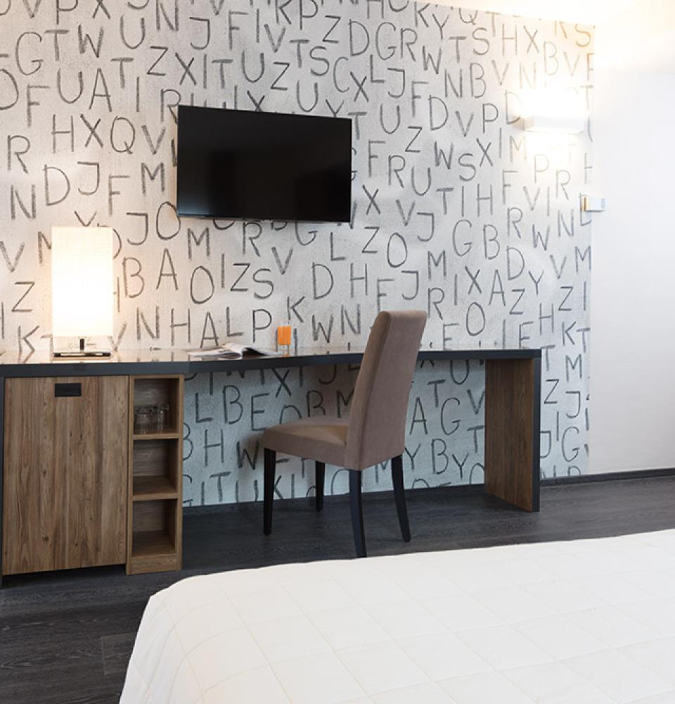 Chambre moderne avec bureau, TV et mur décoré de lettres.