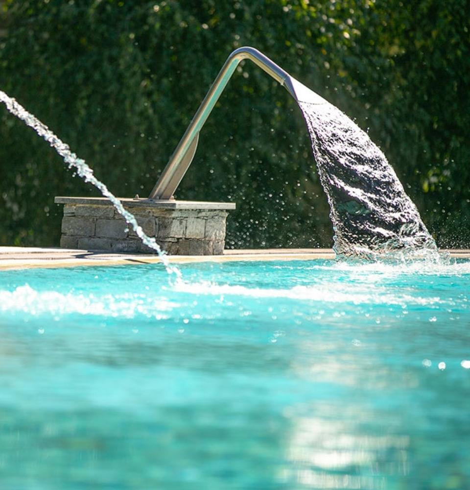 Piscina con getto d'acqua a cascata e fontana decorativa.