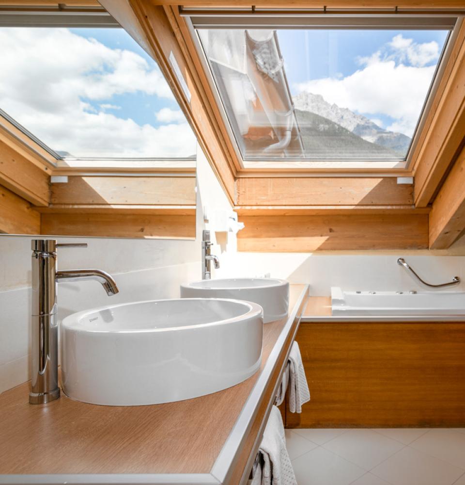 Bagno mansardato con vasca, doppio lavabo e lucernario con vista sulle montagne.