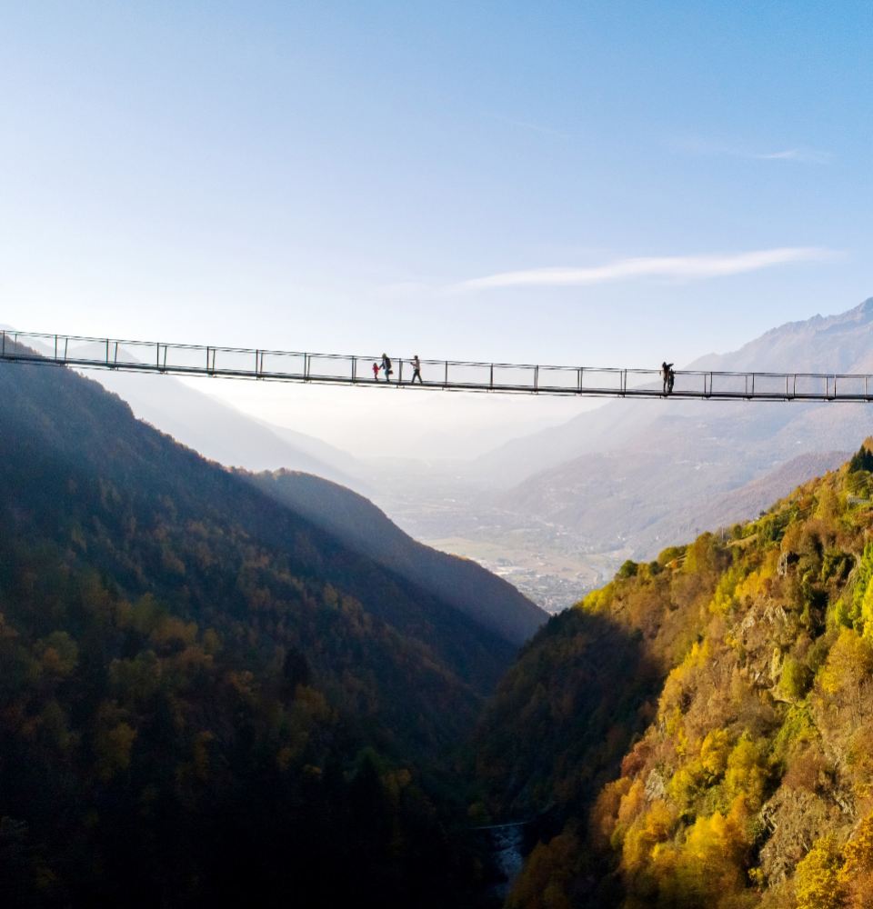 Ponte sospeso tra le montagne con persone che camminano sopra di esso.