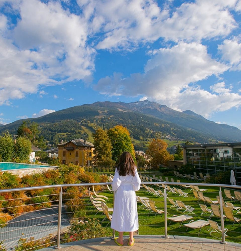 Donna in accappatoio bianco ammira il paesaggio montano da una terrazza panoramica.