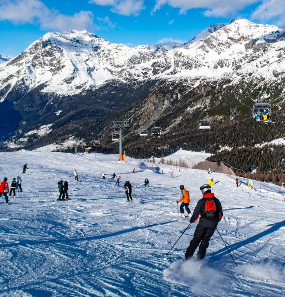 Sciatori sulle piste innevate, circondati da montagne e seggiovie in un giorno soleggiato.