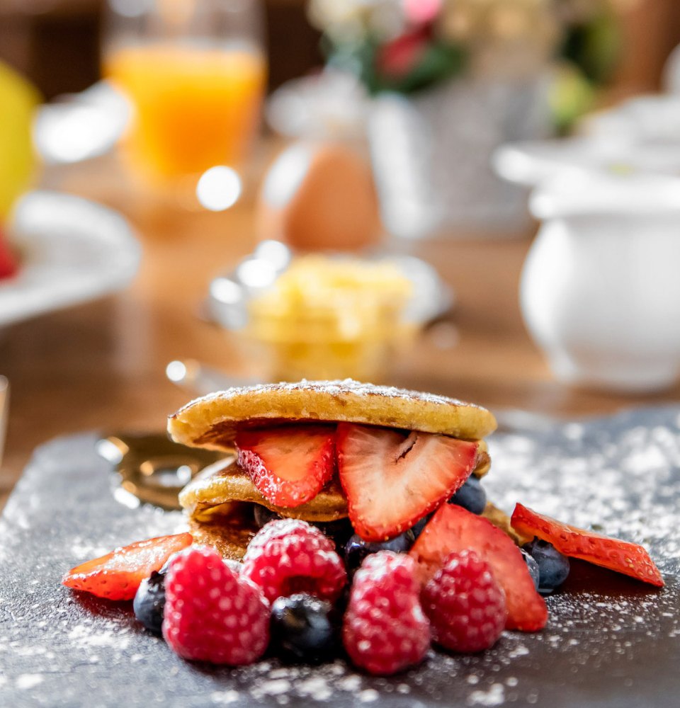 Pancakes con fragole, mirtilli e lamponi, spolverati con zucchero a velo.