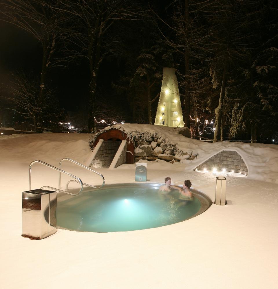 Due persone in una piscina calda all'aperto circondata dalla neve di notte.