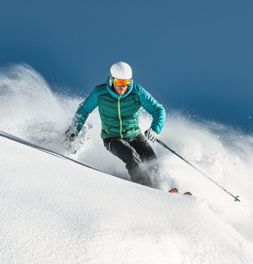 Sciatore in discesa su neve fresca con giacca verde e casco bianco.