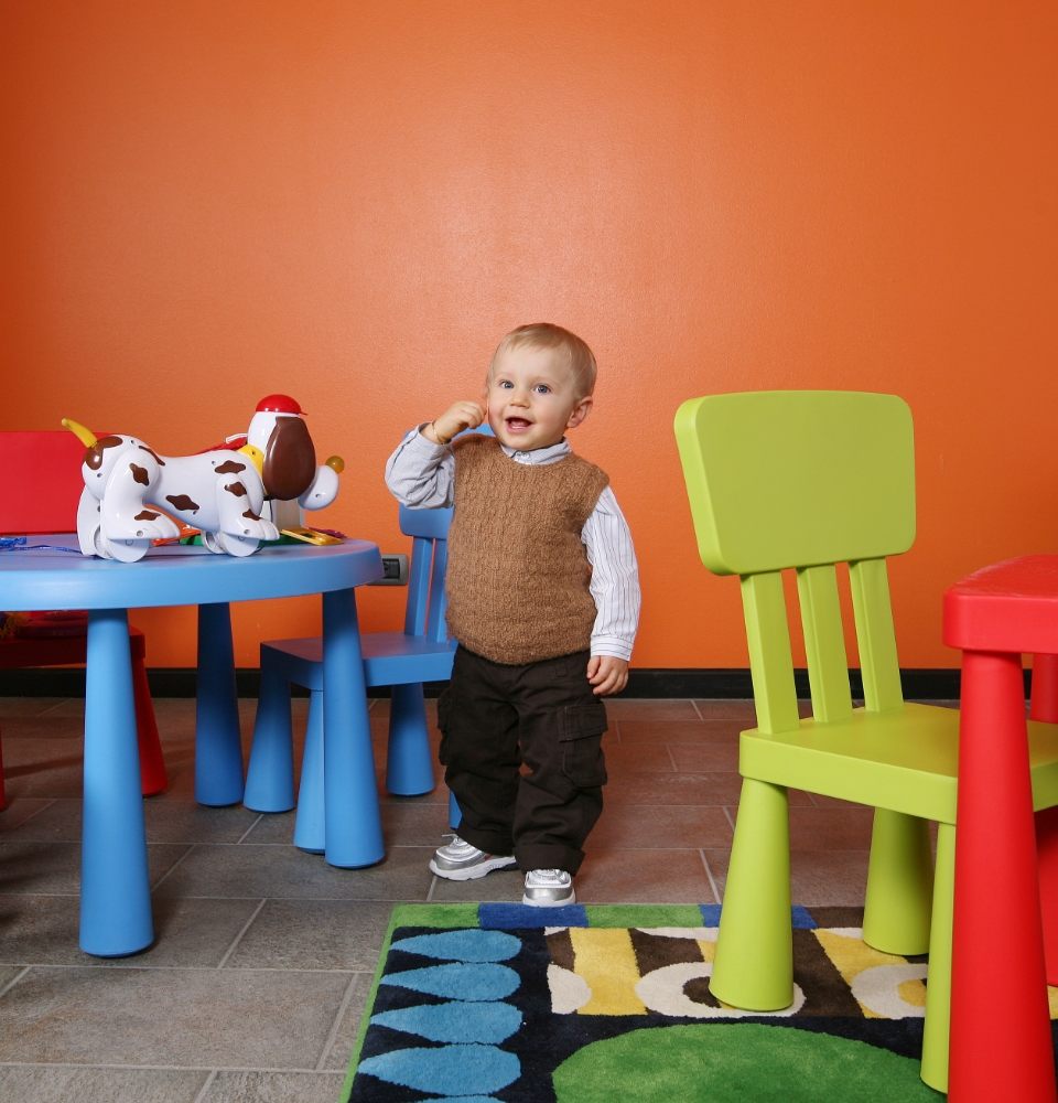 Bambino in piedi in una stanza colorata con sedie e tavolo di plastica.