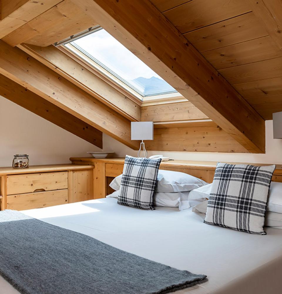 Chambre mansardée avec bois, lucarne et coussins à carreaux.