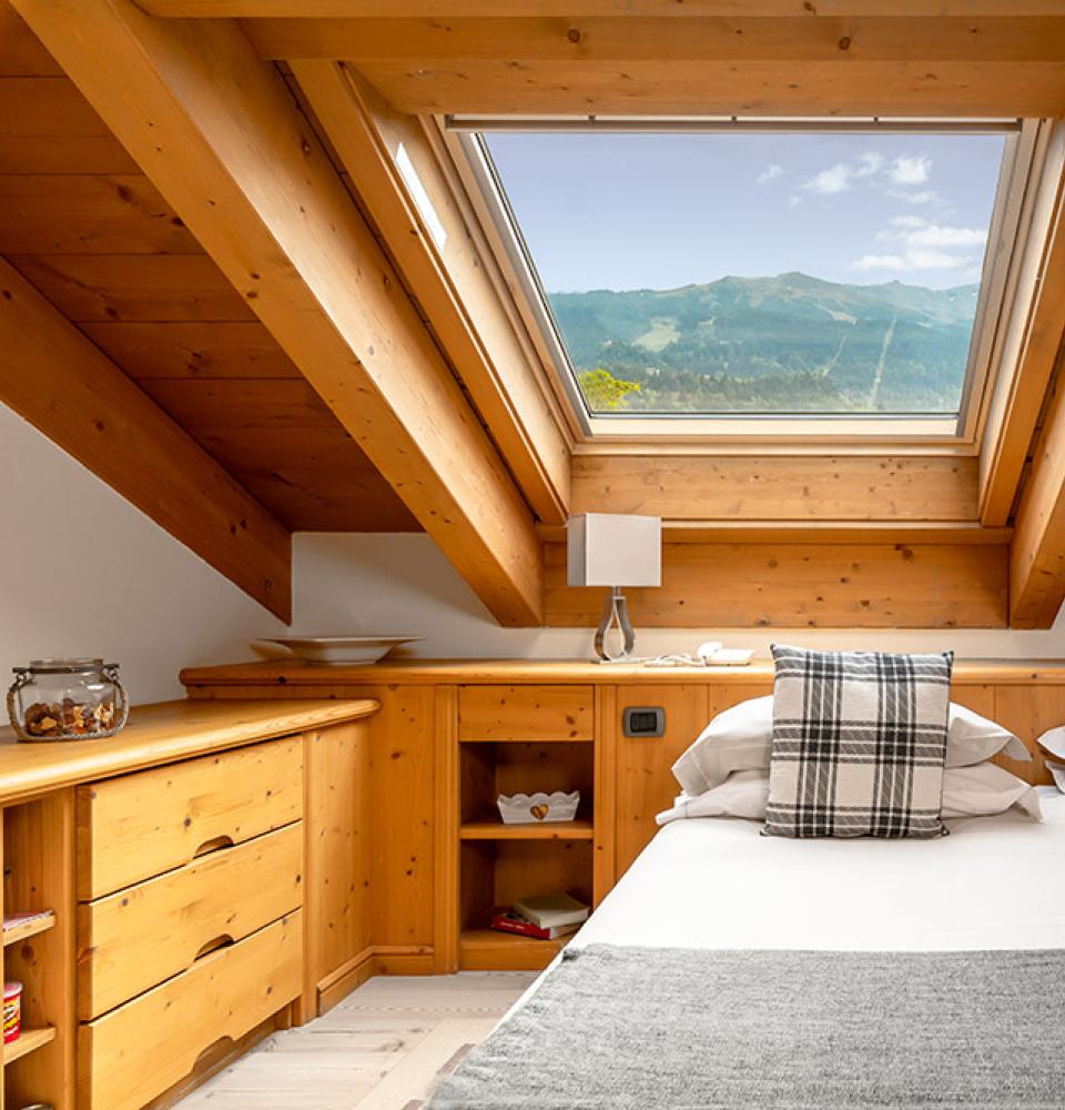 Chambre mansardée avec vue sur la montagne et meubles en bois.