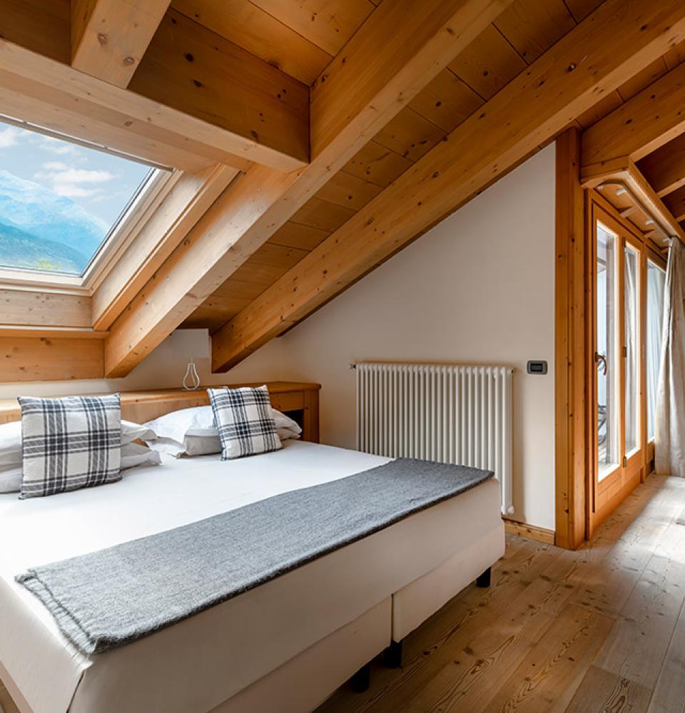 Chambre en bois avec vue montagne, lit double et lucarne.