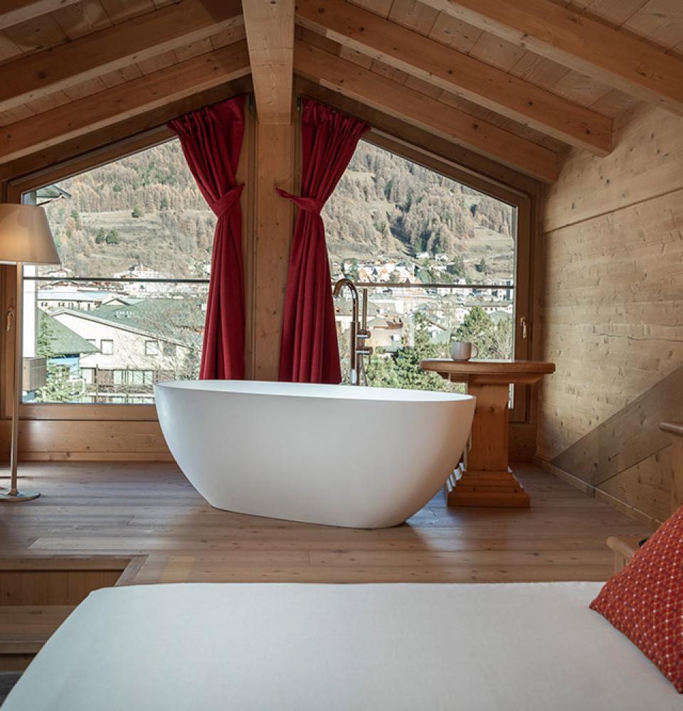 Chambre en bois avec baignoire et vue montagne.