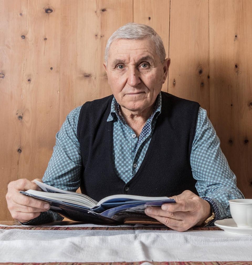 Anziano signore legge un libro seduto al tavolo con una tazza di tè.